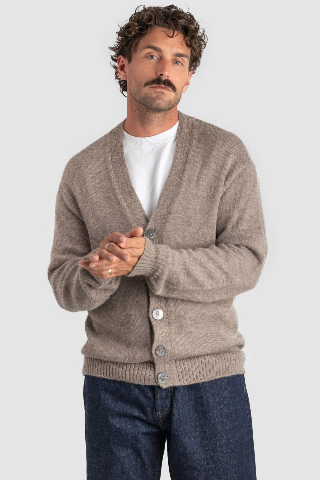 Man wearing a beige cardigan over a white shirt with a plain background #colour_fawn
